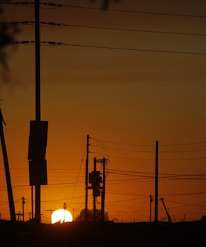 the sun is setting behind power lines and telephone poles